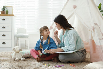 Mother and her daughter drawing in sketchbook together near toy wigwam at home, space for text © New Africa