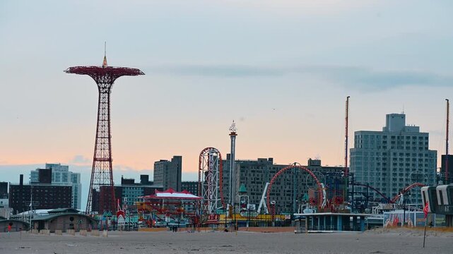 New York, USA, 2 August 2025: Red Parachute Jump tower and Coney Island amusement rides. Wide view of Coney Island beach featuring the historic Parachute Jump and various roller coaster structures.