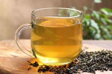 Naklejka premium Refreshing green tea and dry leaves on wooden table, closeup