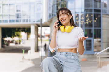 Fototapeta premium Young woman enjoying phone call with casual style, yellow headphones, and smiling expression on city street