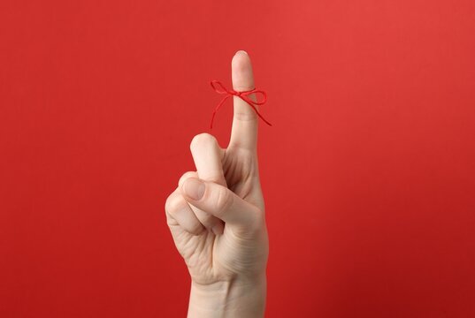 Woman showing index finger with tied bow as reminder on red background, closeup