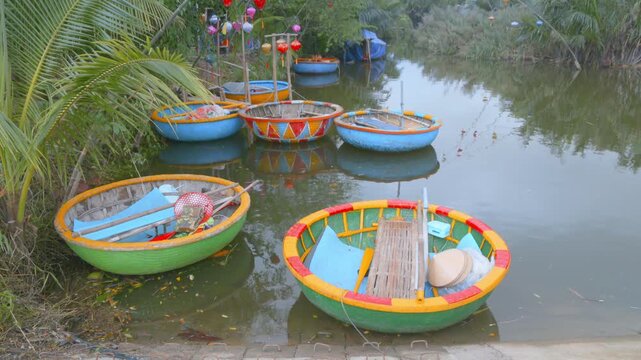 A collection of colorful coracle fishing boats sit on the river in Hoi An, Vietnam. These boats are used by local fisherman to navigate the waterways.