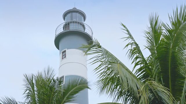 A low angle shot of the historic Cua Dai Lighthouse in Hoi An, Vietnam, surrounded by palm trees against a cloudy sky.