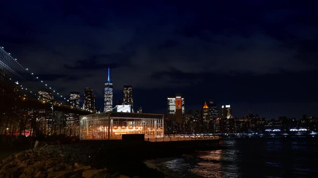 New York, USA, 2 August 2025: Illuminated Janes Carousel and Manhattan skyline at night. Glass pavilion of carousel on DUMBO waterfront with Brooklyn Bridge and city lights in background.