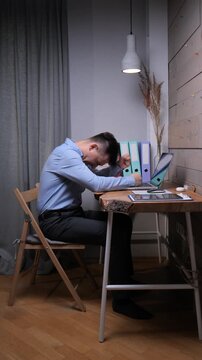 Vertical video young man sitting at a desk, struggling with stress and exhaustion, pulling at his hair in a moment of frustration and despair over his demanding workload and pressures