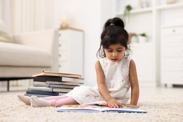 Fototapeta premium Cute little girl reading book on floor at home. Space for text