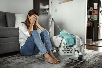 Obraz premium Exhausted woman sitting on floor next to laundry basket feeling overwhelmed by housework, domestic stress and burnout concept 