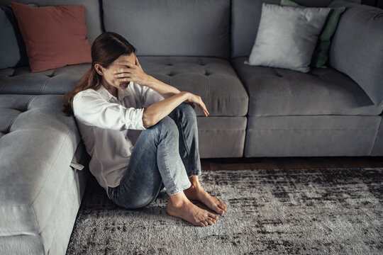 Stressed woman sitting on floor covering face overwhelmed by mental health anxiety burnout depression and emotional fatigue at home
