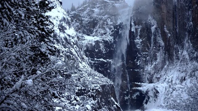 Yosemite National Park Icefall majestic scene. Silent power of frozen water cascading through snowcovered canyons. Imposing icy waterfall carving through rugged snowdusted cliffs under winter sky