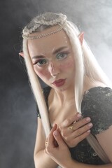 Fototapeta premium Beautiful girl dressed as elf on black background with smoke