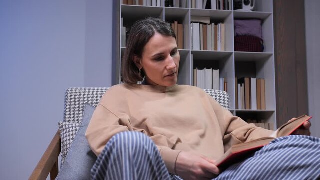 Woman enjoying a quiet moment, comfortably sitting in an armchair with a classic book in her hands, finding joy and knowledge through reading in a personal library setting