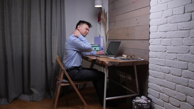 Man rubbing his neck in a home office, showing neck pain and muscle soreness from long hours at a laptop, poor posture and sedentary remote work strain