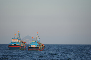 Fototapeta premium Traditional blue and red wooden fishing vessels at sea with a mountain silhouette in the background