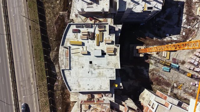 The scene shows a large construction site with ongoing work. Several cranes are in use, and construction materials are scattered around. The location is near a busy road.