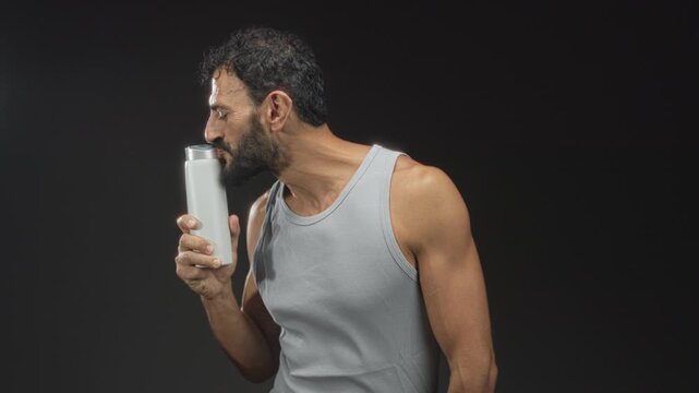 Man holding a white shampoo bottle, smiling and leaning to sniff the cap in studio; curiosity refreshment.