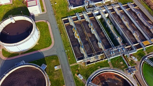 A view of a water treatment facility with several large circular tanks and rectangular processing units. Workers and machinery are visible, indicating ongoing operations.