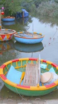 A collection of colorful coracle fishing boats sit on the river in Hoi An, Vietnam. These boats are used by local fisherman to navigate the waterways.