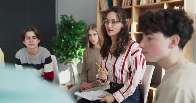 Teens with teacher counselor in classroom discussion. She leads a group session fostering sharing and listening as students empathize to support mental health. Strong teen group help concept.