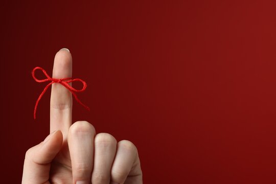 Woman showing index finger with tied bow as reminder on dark red background, closeup. Space for text