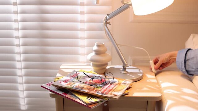 Woman putting lifestyle magazine and glasses onto wooden bedside table at home, closeup