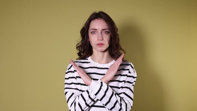 Stop gesture. Woman crossing arms on yellow background