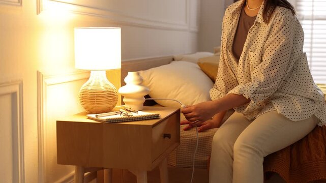 Woman turning on lamp on bedside table at home, closeup. Camera moving forward