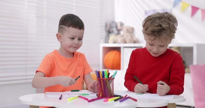 Cute little boys drawing with felt tip pens at white table indoors