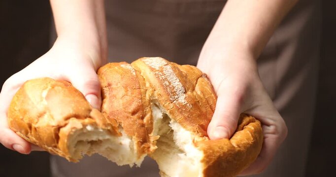 Woman breaking loaf of fresh bread on dark background, closeup