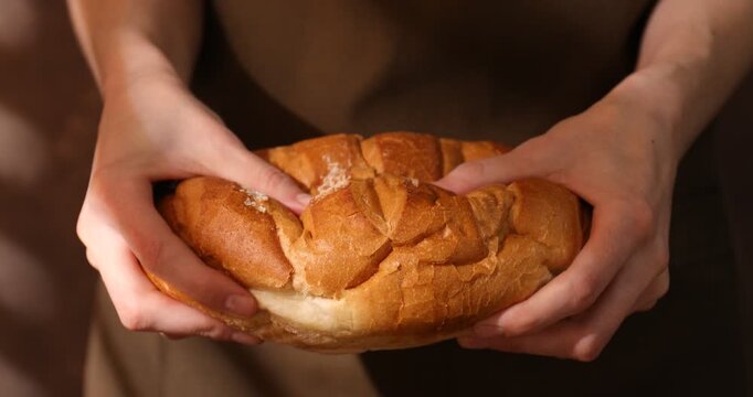 Woman holding loaf of fresh bread on brown background, closeup