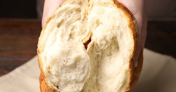 Woman breaking loaf of fresh bread at table, closeup