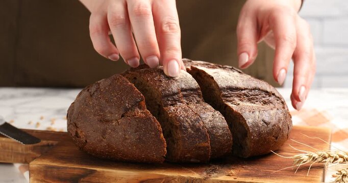 Woman cutting fresh bread at at table, closeup