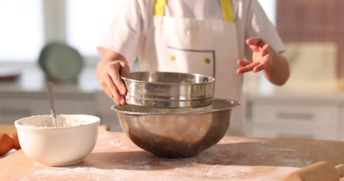 Child sifting flour into bowl with dough at wooden table indoors, closeup
