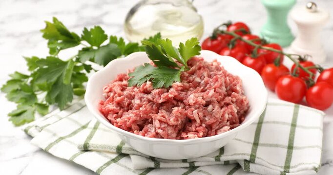 Woman putting parsley onto raw minced beef at white marble table, closeup