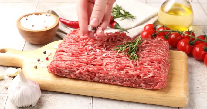 Woman putting salt onto raw minced meat at light tiled table, closeup