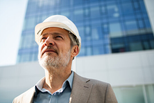 Senior architect in hard hat outside modern office building