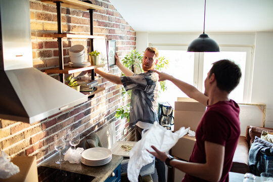 Two men unpacking boxes and decorating kitchen in new apartment