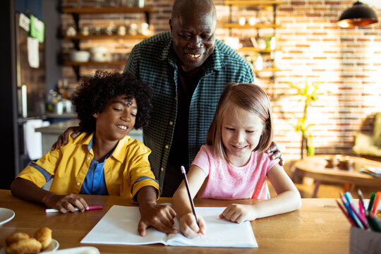 Grandfather helping children with homework at kitchen table