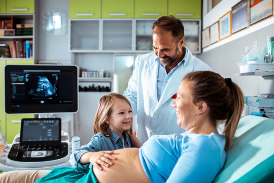 Doctor performing prenatal ultrasound with mother and child in clinic
