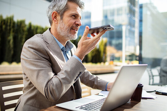 Mature businessman using voice assistant at outdoor cafe