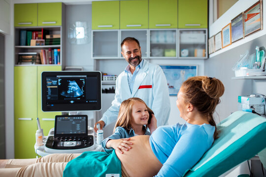 Doctor performing prenatal ultrasound for pregnant mother with daughter at clinic