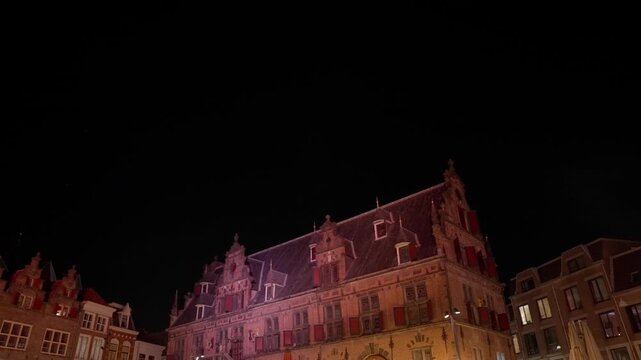 Majestic low-angle night view of the historic "De Waagh" building on Grote Markt, Nijmegen. Its grand facade is beautifully illuminated against the deep dark evening sky, highlighting architectural...