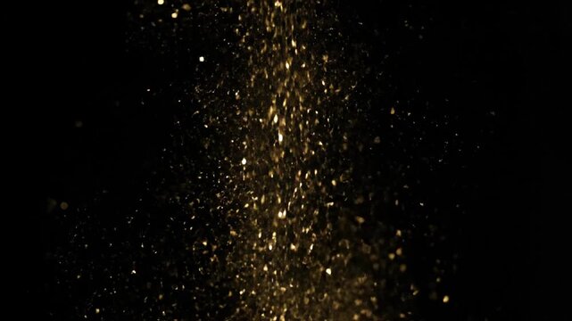 Golden glitter particles falling against a black background, abstract celebration effect