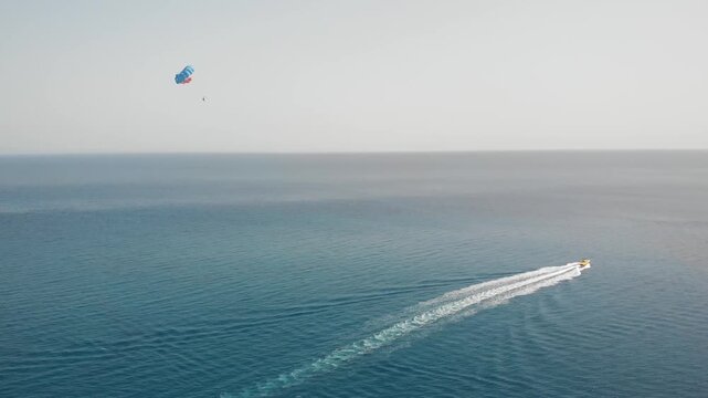 Aerial view of motor boat pulling colorful parachute for parasailing over blue ocean water in summer.