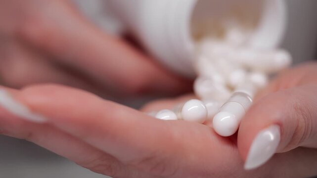 Close up of female hands pouring white capsules into palm on clean background representing medication intake treatment and healthcare concept.