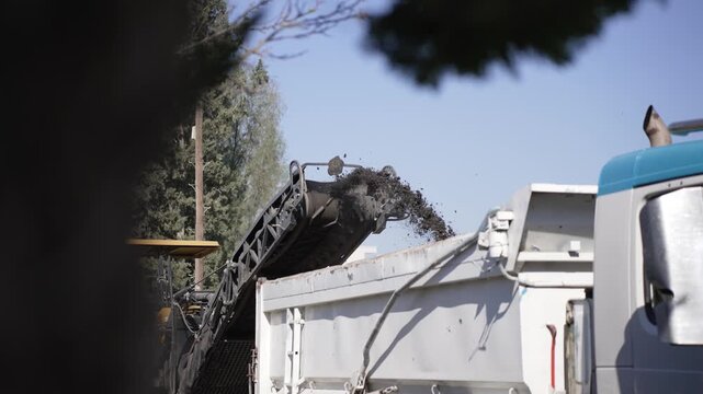 Road material milling machine loading asphalt into dump truck for recycling