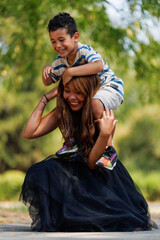 Playful moment between a smiling young boy sitting on a woman's shoulders outdoors © Nikola Spasenoski