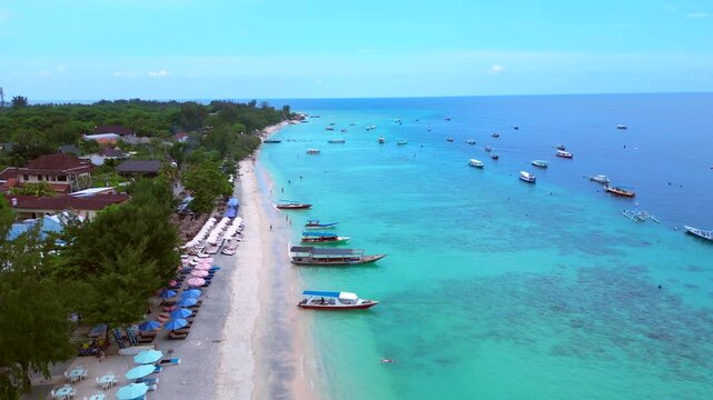 Gili trawangan coastline showing moored boats on turquoise water and sandy beach. Nice aerial view descending panorama overview drone
