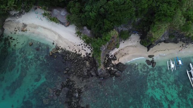 Top down drone view of traditional Bangka boats on tropical beach at Apo Island Philippines with turquoise water and coastal cliffs. Cinematic 4K aerial ideal for travel and island content.