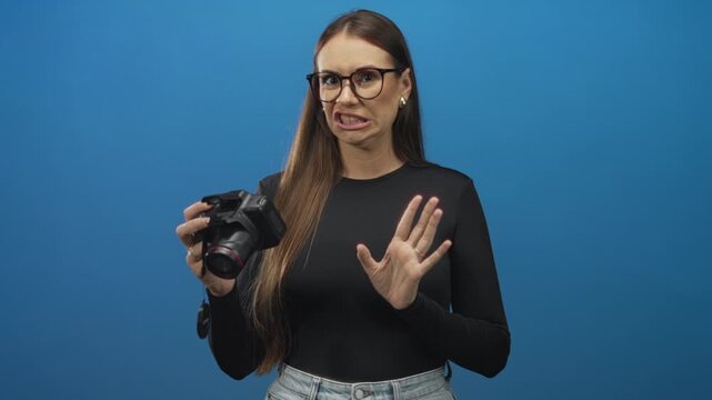Woman holding dslr camera with raised hand and grimacing face showing disgust while checking lens in studio; disgust rejection.