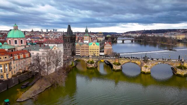 Aerial panorama of Charles Bridge crossing the Vltava in Prague with iconic rooftops and towers under cloudy weather; perfect for tourism marketing, travel guides and architecture editorials
